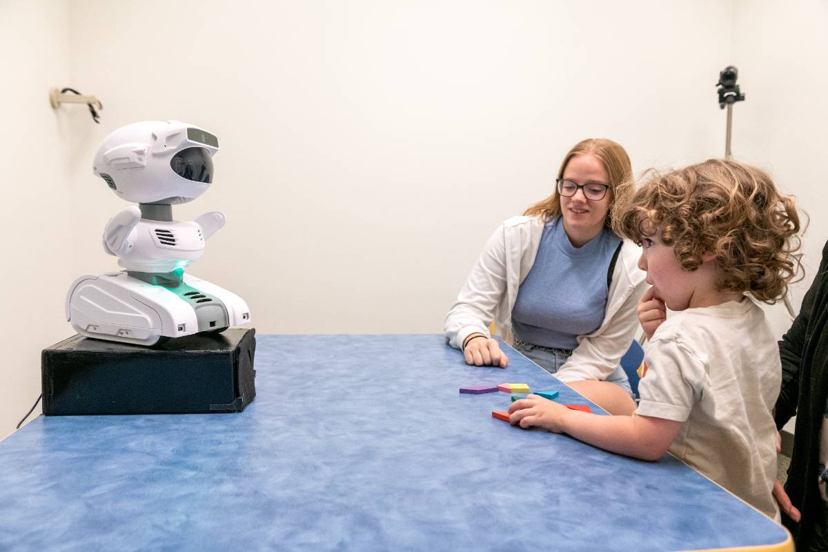Student researcher instructs child subject with help of robot.