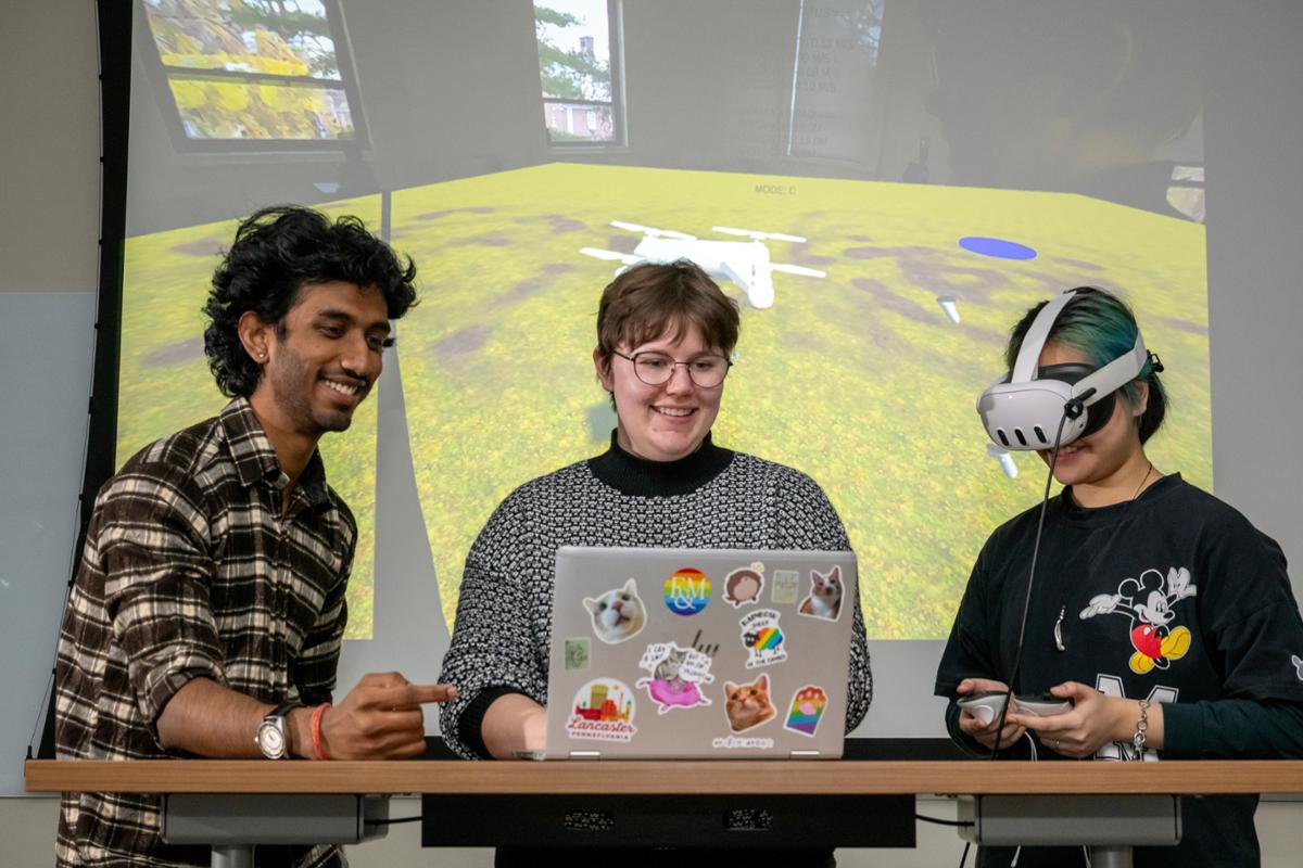 Sujal Shah ’27; Emily Jensen, assistant professor of computer science; and Kha Nguyen ’28 demonstrate their extended-reality program teaching safe piloting of drones.