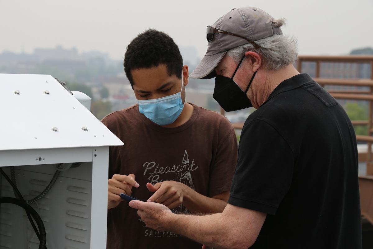 Professor of Geosciences Robert Walter '75 and Julian Marsh '28 monitor Lancaster’s air-quality index via a sampler machine atop of the Alumni Sports & Fitness Center.