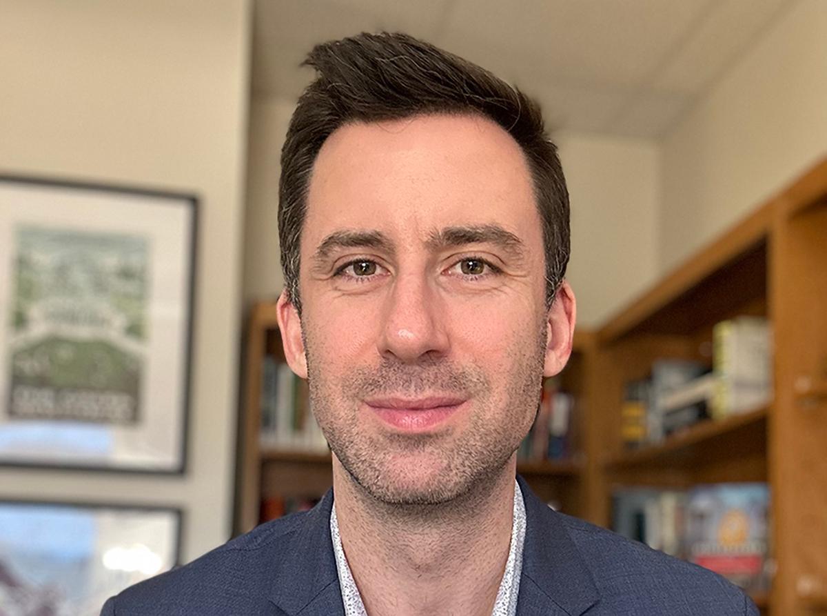 A person smiling in front of a book case.