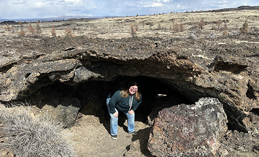 A photo of Karen Mertzman hunched over in the mouth of a cave. 