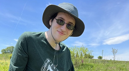 A photo of a person wearing a hat and sunglasses in a field