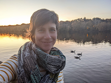 A person pictured in front of a lake with ducks in crepuscular moment. 