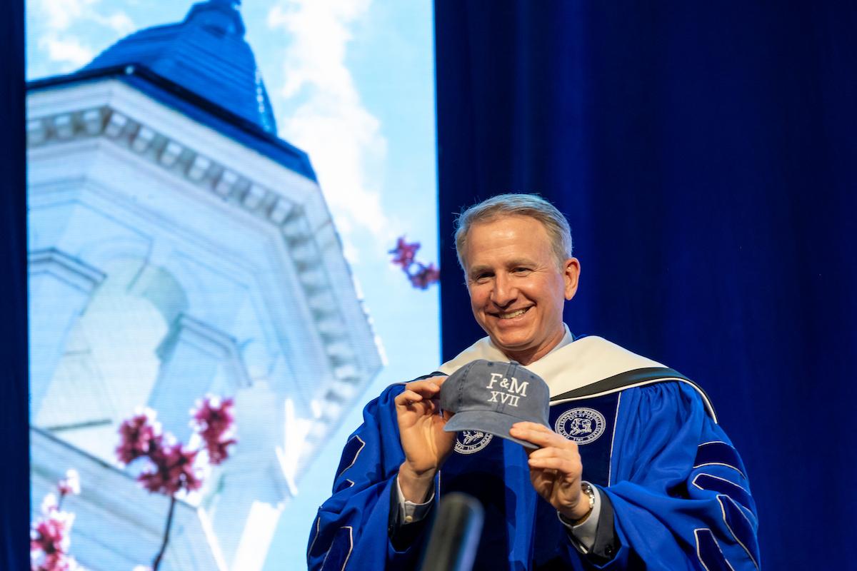 President Rich holds a gifted a hat embroidered with “17” in Roman numerals. (Photo by Deb Grove)