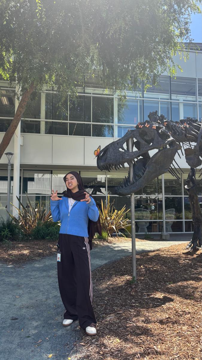 Shahina Tojieva ’25 poses with "Stan," a bronze Tyrannosaurus Rex skeleton replica outside the Googleplex (Google's corporate headquarters).