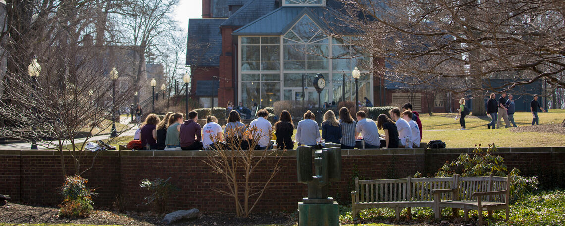 Students take advantage of the unusually warm weather. The campus coffee shop and spires of Old Main are visible in the background.
