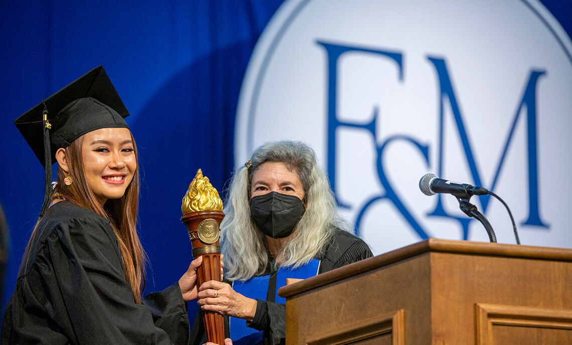 Lisa Brooks '85, president of the Alumni Association, ceremoniously passes the torch to newly minted graduate Trinity Nguyen, president of the Class of 2022.