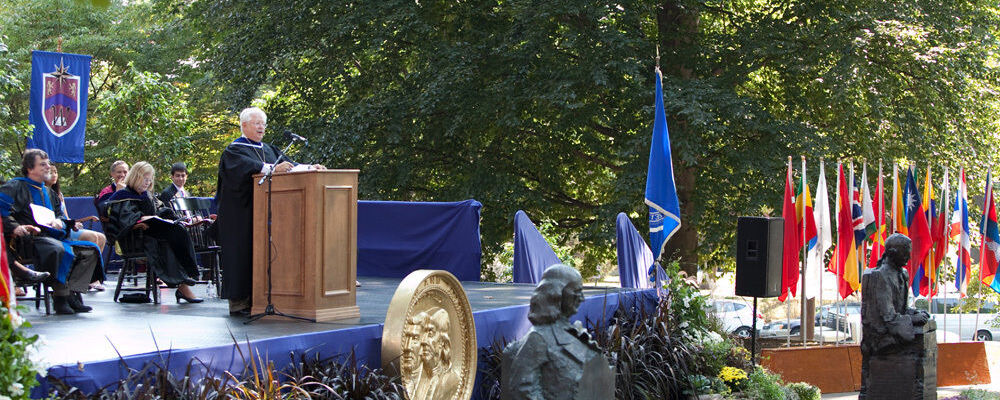 Interim President John F. Burness '67 presents his Convocation remarks, flanked by statues of Benjamin Franklin and John Marshall in their new locations on Manning Alumni Green.