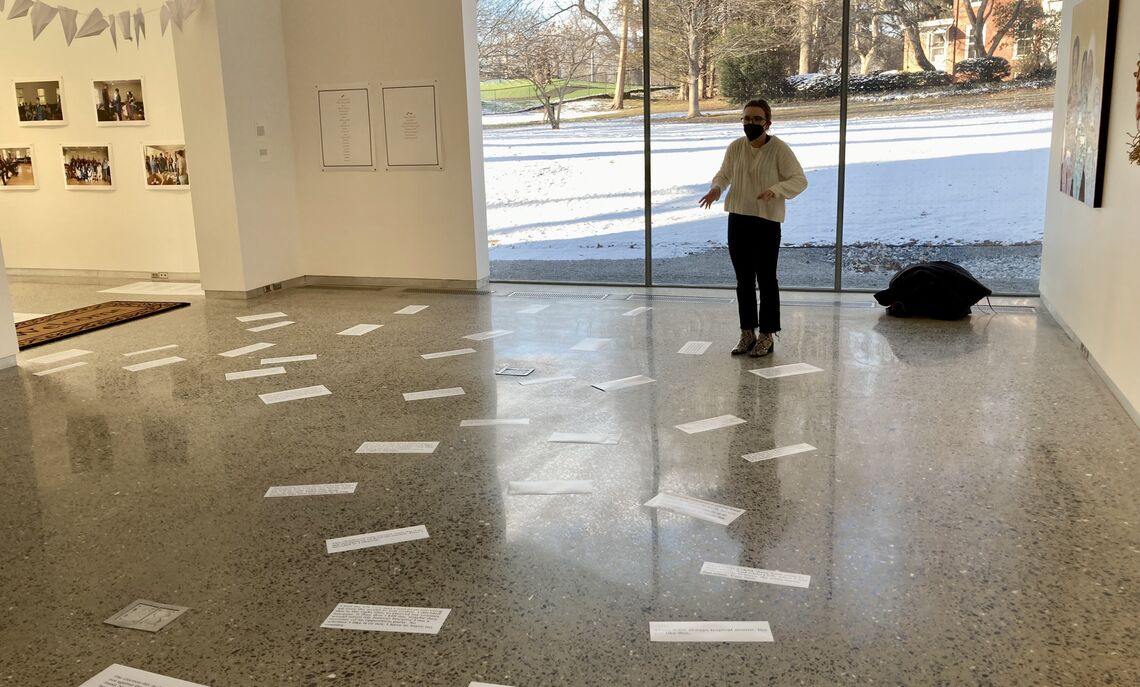 Senior Michele Jacobs before the tiles of quotes taken from several years of student interviews with refugees and immigrants who came to Lancaster.