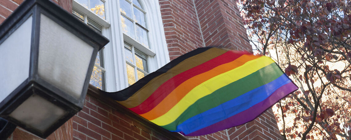 A "more color, more pride" LGBTQ flag hangs from a window of Goethean hall, moving with the wind.